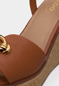 Bruine leren sleehaksandaal met gevlochten plateauzool en gouden decoratieve gesp op de teband.