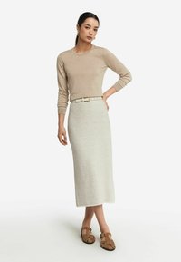 Beige stickad tröja med långa ärmar, tillsammans med en ljusgrå knuten tygkjol och bruna sandaler med remmar. Enkel bältesdetalj på kjolen.