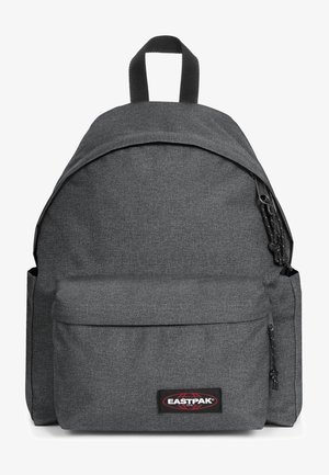 Mochila de tela gris con una parte superior redondeada, bolsillo frontal con cremallera y correas de hombro ajustables. Cuenta con una etiqueta de marca negra en la parte delantera.