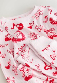 Lyserød ribstrikket sweater med røde grafiske motiver af hjerter, sløjfer og pile; afsluttet med en blød rund hals og ribstrikkede ærmegab.