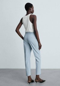Pantaloni su misura azzurri con vestibilità slim, dotati di una vita a media altezza e due tasche posteriori. Abbinati a un top bianco senza maniche.