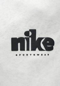 Μαύρο λογότυπο Nike σε λευκό φόντο ύφασματος, με έντονα γράμματα και τη λέξη "SPORTSWEAR" σε μικρότερα γράμματα από κάτω.