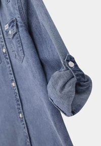 Denimowa koszula w jasnoniebieskim kolorze z zapięciem na guziki z przodu, dwoma kieszeniami na piersi oraz podwiniętymi rękawami z guzikowymi akcentami.