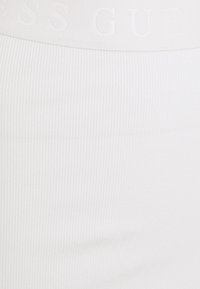 Biały prążkowany materiał o gładkiej fakturze, z pionowym wzorem i wytłoczonym logo "Guess" na pasku talii.