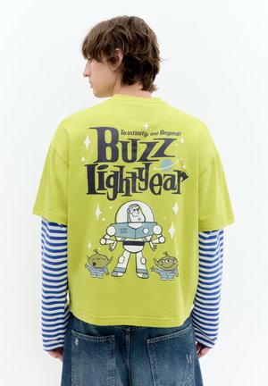 Personne portant un t-shirt vert citron Buzz l'Éclair avec des personnages de dessin animé et le texte "To infinity, and Beyond!" visible dans le dos.