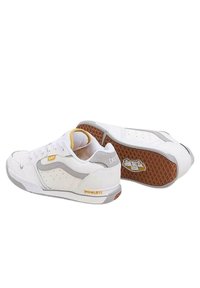 Zapatillas deportivas blancas con acentos en gris y amarillo, que presentan una suela de goma texturizada, lados perforados y un acolchado en el collar para mayor soporte.