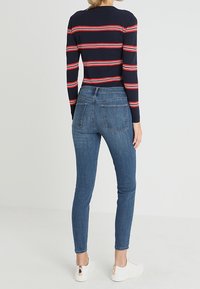 Marinrandig långärmad topp med röda och vita ränder, matchad med åtsittande blå denimjeans och vita sneakers. Slät textur och strömlinjeformat passform.