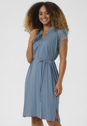 Vestido azul de tejido suave, con escote en v, lazo en la cintura y mangas cortas de encaje. El dobladillo tiene aberturas laterales para un detalle adicional.
