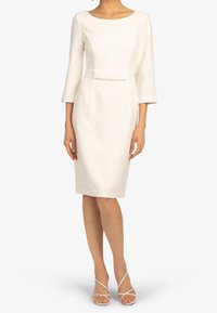 Biała sukienka do kolan z rękawami o długości trzy czwarte, dopasowanym topem i paskiem w talii. Gładka faktura, minimalistyczny design.