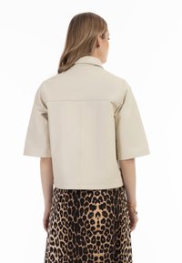 Jachetă din piele bej, scurtă, cu mâneci scurte, textură netedă și un guler simplu, asortată cu o fustă cu model leopard.
