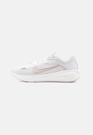 Witte Nike hardloopschoen met gouden swoosh, bovenwerk van mesh en dikke, met kussen gevulde zool met het label "ComfiRide", zijaanzicht op een witte achtergrond.