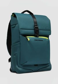 Türkisfarbener wasserdichter Rucksack mit strukturiertem Design, verstellbaren Riemen, vorderer Reißverschlusstasche mit neon-gelben Akzenten und einer oberen Klappe als Verschluss.
