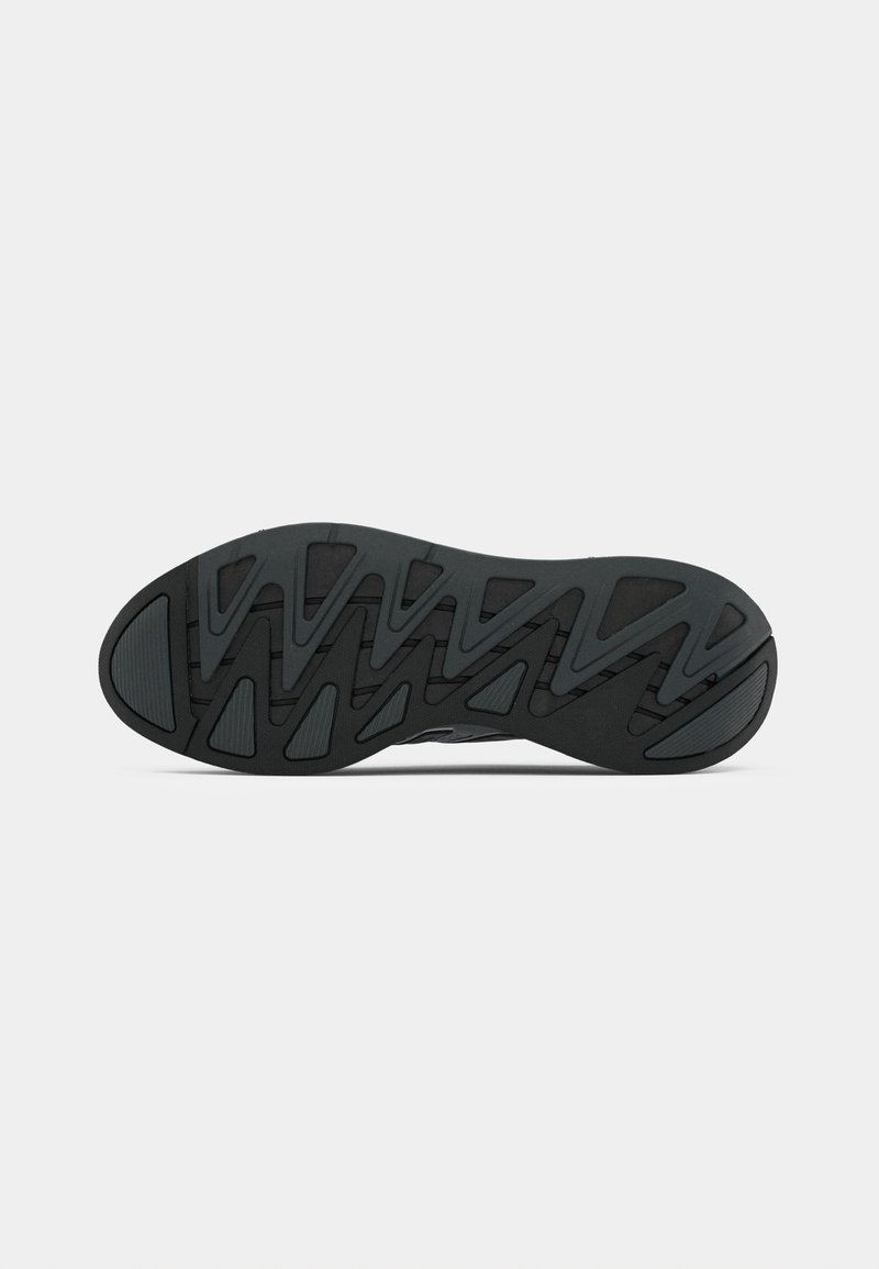 Schwarze Schuhsohle mit geometrischem Zickzack- und dreieckigem Profildesign auf einem schlichten weißen Hintergrund.