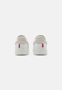 Białe sneakersy z gładką skórzaną cholewką, z zamszowymi akcentami i białą gumową podeszwą. Posiadają małą czerwoną metkę logo na heel.