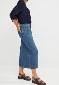 Culotte in denim blu medio con vita alta, gamba ampia e tasche laterali. Abbinato a una blusa blu navy e sandali marroni.