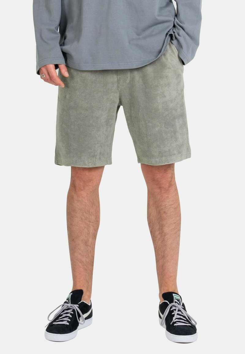 Green suede shorts with a soft texture, featuring a casual fit and paired with black sneakers with white soles and gray laces.