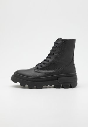 Zwarte leren veterschoenen met een gestructureerde afwerking, ronde neus en stevige rubberen zool met uitgesproken profielpatronen.