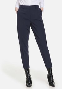 Granatowe, dopasowane spodnie o klasycznym kroju, z wyraźnym kantem, dwiema bocznymi kieszeniami i pętelkami na pasek, w połączeniu z błyszczącymi czarnymi botkami na kostkę.