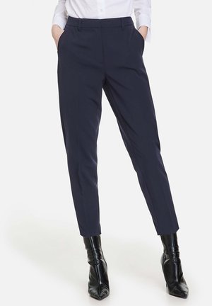 Marineblauwe op maat gemaakte broek met een slim fit, scherpe plooi, twee zijzakken en riemlussen, gecombineerd met hoogglanzende zwarte enkellaarzen.