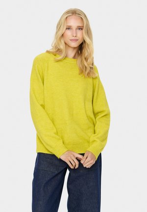 Gul pullovertröja med rund halsringning och ribbade ärmslut, ihop med mörkblå vida jeans. Mjuk textur och avslappnad passform.