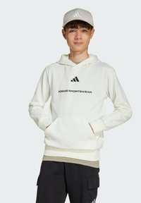 White hoodie with front pocket, Adidas logo in black, soft fabric, fitted cuffs, and a drawstring hood; worn over black pants.