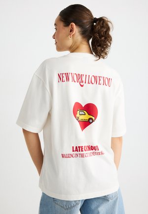 Λευκό βαμβακερό t-shirt με κόκκινες γραφικές εκτυπώσεις: «NEW YORK I LOVE YOU» και μια καρδιά με ένα κίτρινο ταξί. Χαλαρή εφαρμογή, κοντά μανίκια, casual σχεδίαση.