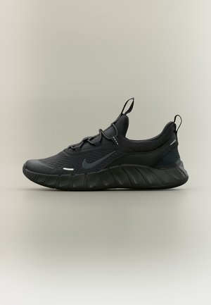 Chaussure de sport Nike noire avec empeigne en mesh, semelle épaisse et amortie, et languettes d’accroche sur la languette et le talon, présentée en profil sur fond neutre.
