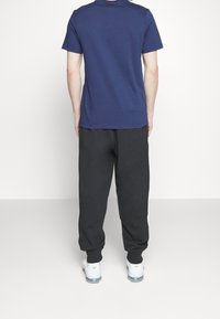 Marinblå t-shirt med kort ärm som är kombinerad med svarta sweatpants, båda tillverkade av bomull. Byxorna har elastiska muddar och fickor.