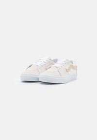 Baskets en daim beige et cuir blanc avec lacets blancs, semelle plate blanche, embout perforé et une bande accentuée couleur fauve sur le côté.