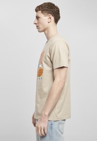 Beige bomull t-skjorte med grafisk design som viser en basketball og en tegneseriefigur, kort erm, og en avslappet passform.