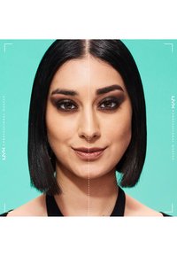 Femme aux cheveux noirs et raides montrant la moitié de son visage avec un maquillage des yeux smoky foncé et l'autre moitié sans maquillage, sur un fond turquoise.