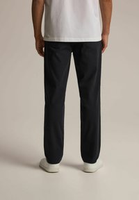 Ciemnoniebieskie spodnie z gładkiego materiału, o prostym kroju nogawki, z dwoma tylnymi kieszeniami, noszone z białymi trampkami.