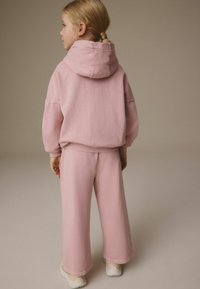 Rosa bomullshuvtröja med stor huva, avslappnad passform och ribbat avslut, i kombination med matchande vida byxor i mjukt material. Vita sneakers.