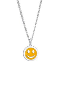 Sølv halskæde med en rund smiley ansigt vedhæng, der har et gult emalje-smil og øjne, hængende fra en snoet kæde.