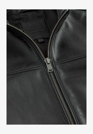 Black leather jacket featuring a silver zipper, textured surface, and a label sewn into the inside with the brand name "NEXT SIGNATURE."