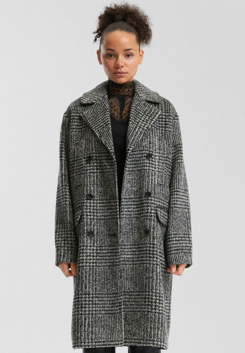 Grijs en zwart geblokt wollen jasje, dubbelzijdig met grote knopen, brede kraag, zijzakken en een gestructureerde stof met een houndstooth-patroon.