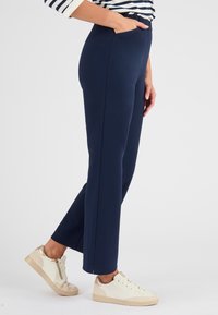 Marineblauwe broek met een recht ontwerp en zijzakken, gemaakt van een gladde stof. In combinatie met lichtgekleurde casual sneakers.