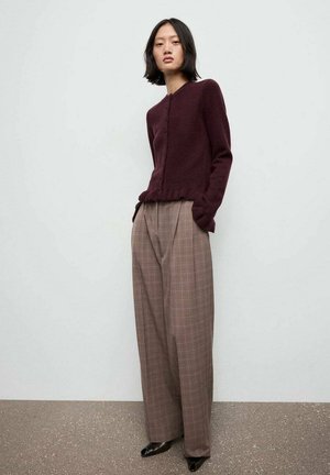 Cárdigan de punto burdeos con cuello redondo y cierre de botones, combinado con pantalones de cuadros de cintura alta y pierna ancha en tonos marrones. Zapatos negros.