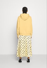 Yellow hoodie with a classic design, paired with a flowy knee-length cream skirt featuring a black tear-drop pattern. Black sneakers complete the look.