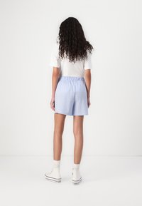 Pantaloni corti azzurri chiari con vestibilità comoda e cintura elastica, realizzati in tessuto strutturato. Abbinati a una maglietta bianca e sneakers bianche.