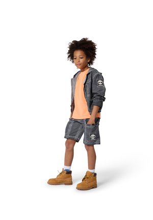 Grijze denim hoodie en korte broek, oranje T-shirt, bruine laarzen. Heeft logopatches en een gestructureerde stof. Witte achtergrond.