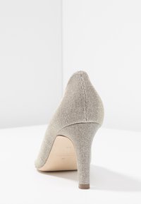 Szpilki z teksturowanym, metalicznym wierzchem w jasnym złocie. Posiadają spiczasty czubek oraz smukły, brązowy obcas.