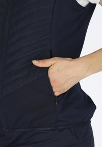 Gilet navy con pannelli trapuntati, zip frontale e tasche laterali. Presenta una texture liscia e un logo discreto all'orlo.