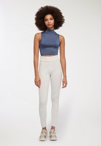 Dopasowany niebieski top typu mock-neck, krótki, zestawiony z jasnoszarymi legginsami o wysokim stanie oraz neutralnymi sneakersami; gładki materiał i bezszwowy krój.