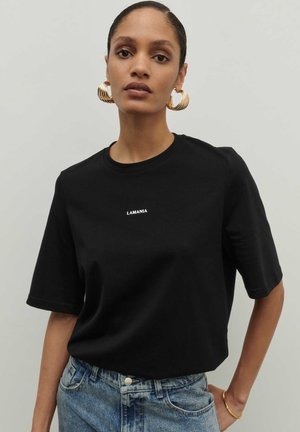 Czarny T-shirt krótki rękaw wykonany z bawełny z okrągłym dekoltem, z białym logo "LAMANIA" z przodu. W komplecie z dżinsowymi spodniami.