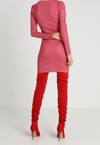 Robe tricotée à manches longues avec des rayures rouges et une silhouette ajustée, associée à des bottes rouges texturées jusqu'aux genoux et des talons hauts.