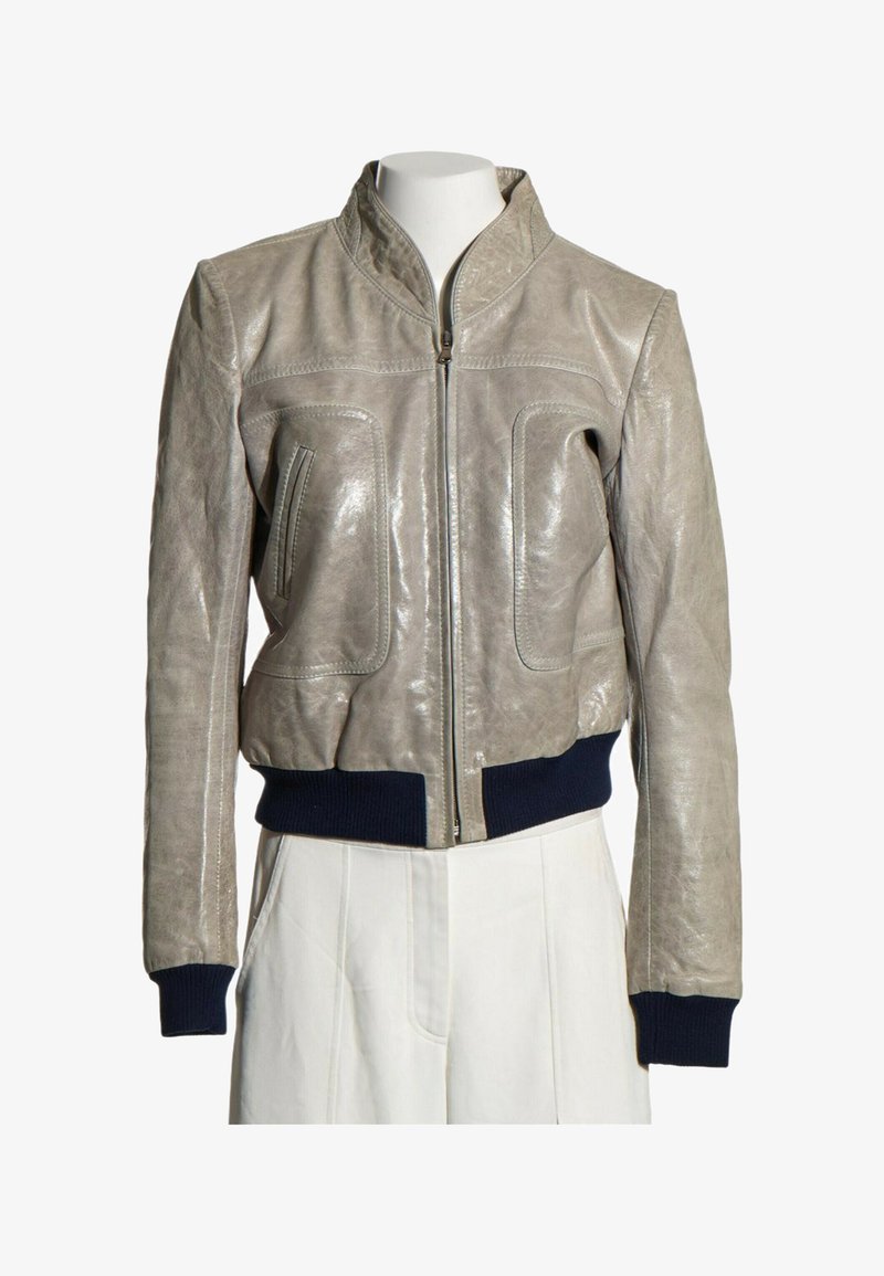 Blouson bomber en cuir gris clair avec fermeture éclair frontale, poignets et taille côtelés bleu marine, présenté sur un mannequin torse portant un pantalon blanc.