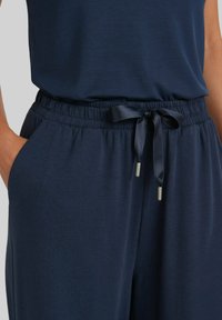 Marineblauwe joggers van zachte stof, met een elastische tailleband met een trekkoord en zijzakken, die een ontspannen pasvorm bieden.