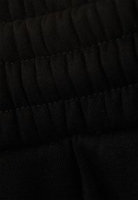 Black elastic waistband with horizontal ribbing and smooth texture, showcasing stitching details and soft draping fabric underneath.