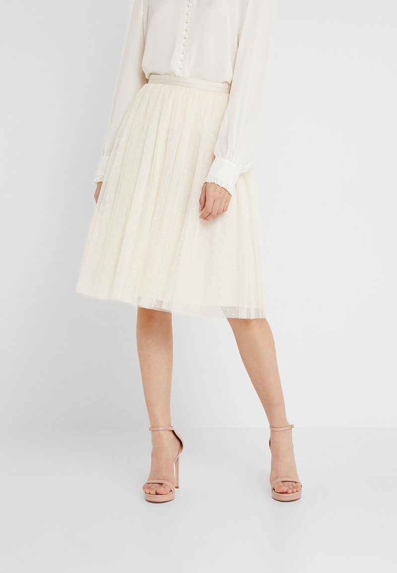 Jupe en tulle crème clair à la silhouette évasée, ornée de motifs à pois et d'une taille élastique, associée à des talons nus à brides.